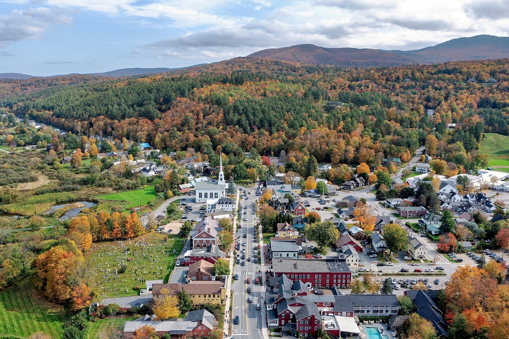 aerial view of Stowe Vermont in early autumn. changing leaves are seen, distant mountains, and a view down main street with its buildings and white steepled church