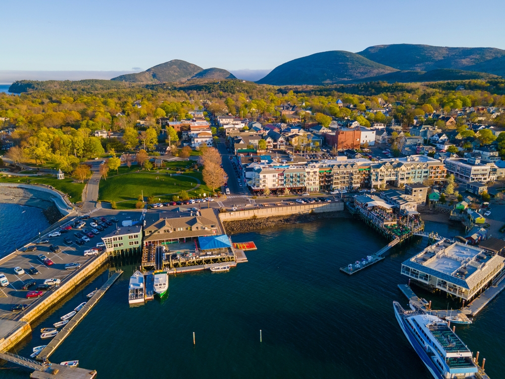 aerial view of bar harbor maine, a marina with boats, a small town, lots of trees, and distant low mountains