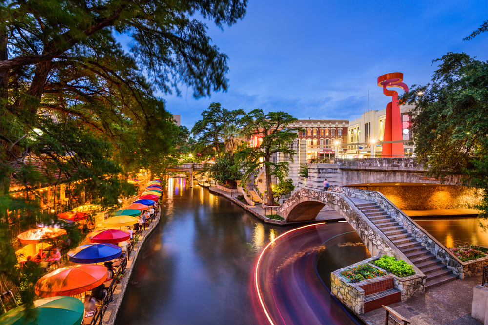 image of the san antonio riverwalk at dusk. Brightly colored umbrellas line a peaceful river overhanging with trees.