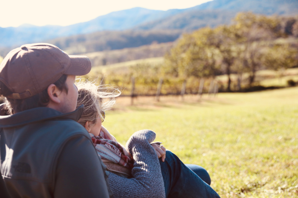 couple sitting leaning on eachother overlooking a field and mountains in early autumn - romantic getaways in Virginia
